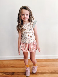 a little girl wearing a ruffle top and shorts