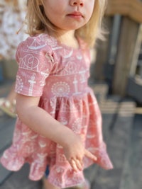 a little girl in a pink dress standing on a deck